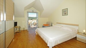 A bedroom with a large bed, a TV, a desk, and a view of a balcony with outdoor furniture. - Apartments Villa Rose - Standard Studio with Sea View Terrace (A2 bijeli) (Sumartin)