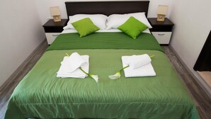 Un lit bien fait, avec une literie verte, des oreillers blancs et un plaid vert. Il y a deux tables de chevet, chacune surmontée d’une lampe et d’une petite boîte en bois.