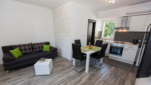 Un espace de vie compact avec un canapé noir, des coussins verts, une petite table blanche et un coin repas avec une nappe verte.