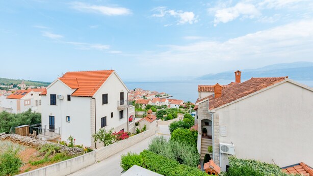 Ein Küstendorf mit terrakottafarbenen Dächern, einem klaren Himmel und Blick auf das Meer.