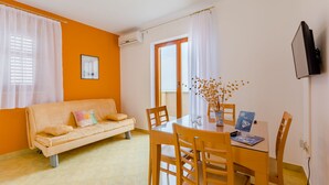 Ein Zimmer mit einer Couch, Esstisch, Stühlen, einem Fernseher und einem Fenster mit Vorhängen.