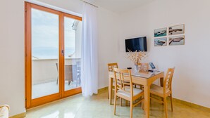 Ein Essbereich mit Tisch und Stühlen, einem an der Wand befestigten Fernseher und Blick durch eine Schiebetür ins Freie.