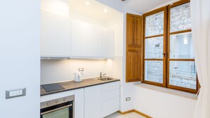 A compact kitchen with white cabinets, a built-in oven, a sink, and a window with a stone wall view.