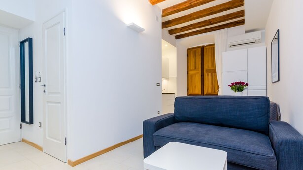 A modern living room with a blue sofa, a white coffee table, and a wooden ceiling beam.