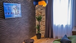A modern living room with a green sofa, a small wooden table, a potted plant, and a wall-mounted TV displaying a map. - Rooms Lejletul - Family Double Room with Square View (Miradž) (Split)