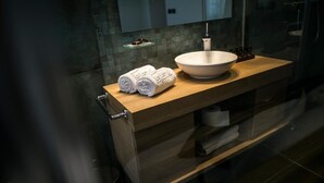 A modern bathroom with a wooden vanity, a large white sink, and a mirror above it. There are rolled towels on the vanity and a small shelf with toiletries. - Rooms Lejletul - Family Double Room with Square View (Miradž) (Split)
