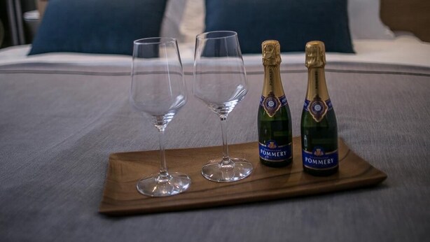 A bed with two pillows, a bedside table with two champagne bottles and two glasses, and a glass wall in the background. - Rooms Lejletul - Family Double Room with Square View (Miradž) (Split)