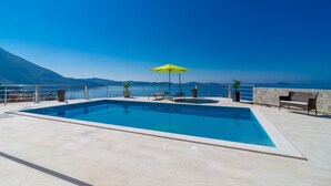 A rectangular swimming pool with a yellow umbrella, surrounded by a stone deck and potted plants.