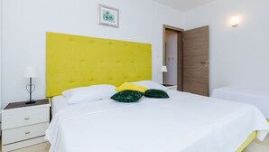 A hotel room with a yellow headboard, white bedding, and a bedside table with a lamp.