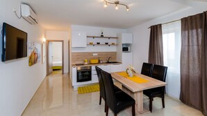 A modern kitchen with white cabinets, a built-in oven, and a microwave. There is a dining table with black chairs and a yellow placemat.