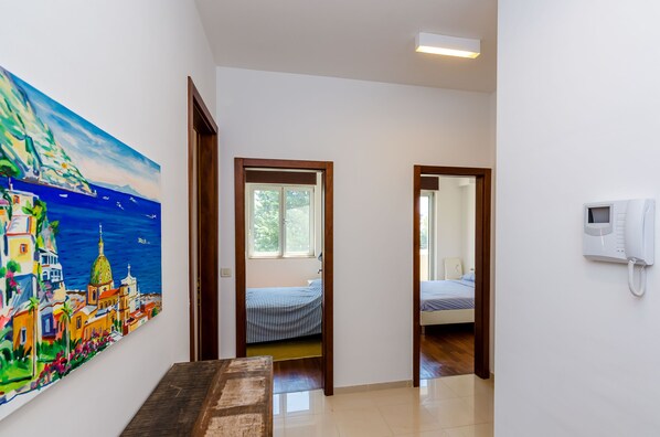 A hallway with a painting of a coastal city, a bed with striped bedding, and a telephone on the wall.