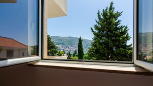 Ein Fenster mit Blick auf Berge, Bäume und eine ferne Stadtansicht.