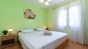 A bedroom with two beds, a nightstand with a lamp, a painting on the wall, and a window with curtains.