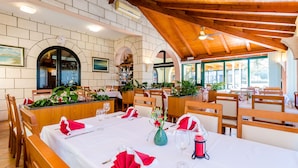 Ein Restaurant mit Holzbalken, weißen Wänden und Rundbogenöffnungen. Die Tische sind mit roten Servietten und weißen Tischdecken gedeckt.