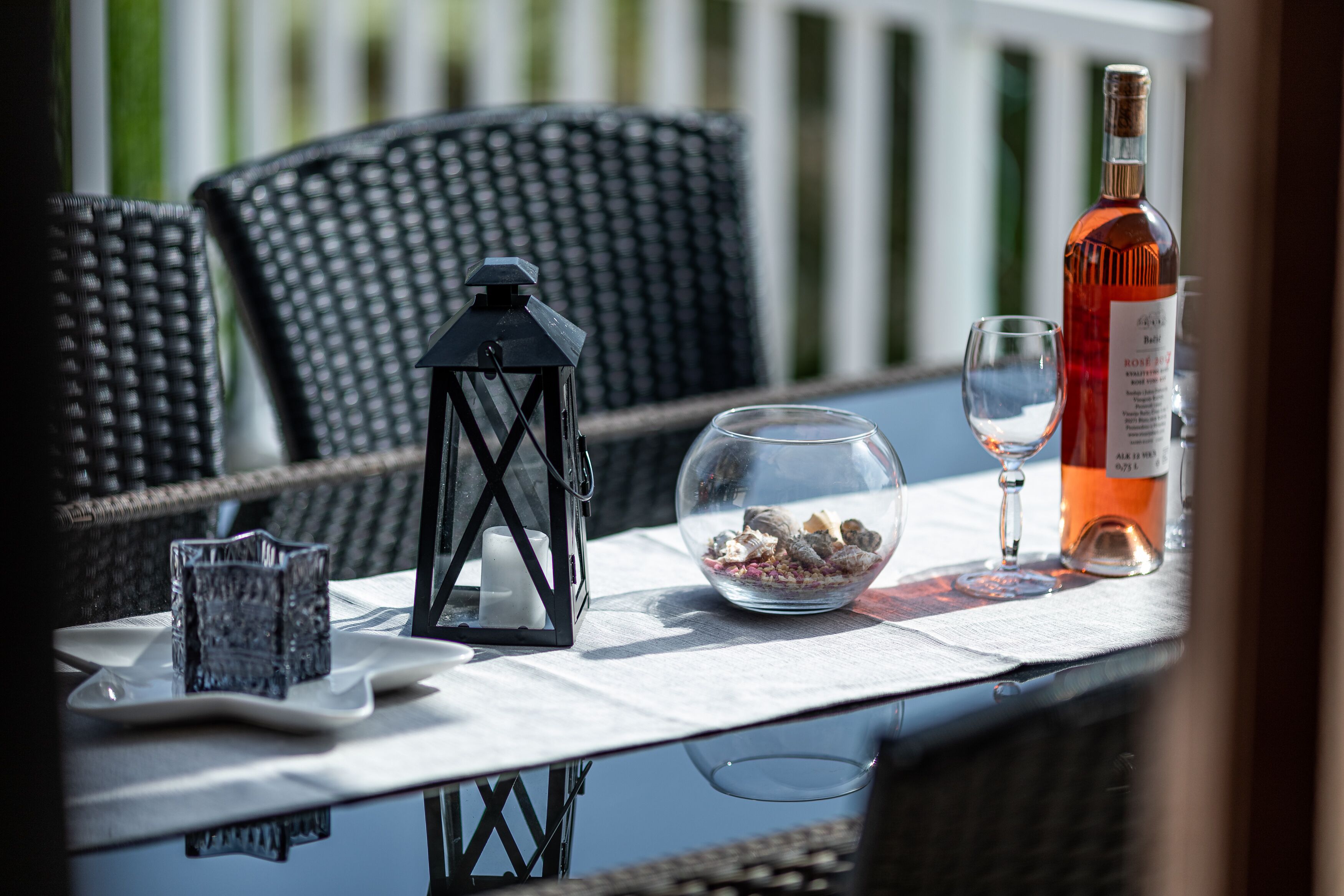 A table with a bottle, a glass, a lantern, and a bowl of pebbles.