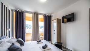 Una habitación de hotel con una cama grande, un televisor montado en la pared y un balcón con cortinas.