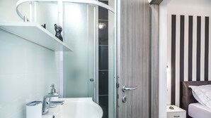 Un baño moderno con un lavabo blanco, cabina de ducha de vidrio y una puerta de madera.