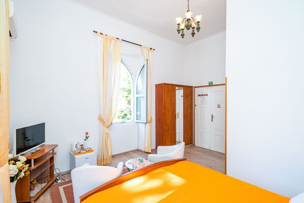 A hotel room with a bed, a TV, a small table with flowers, a wooden cabinet, and a window with curtains.