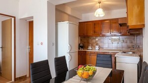A compact kitchen with wooden cabinets, a white refrigerator, and a dining table with a fruit bowl. - Apartments Nena (ST) - One Bedroom Apartment with Terrace and Sea View (Pisak)