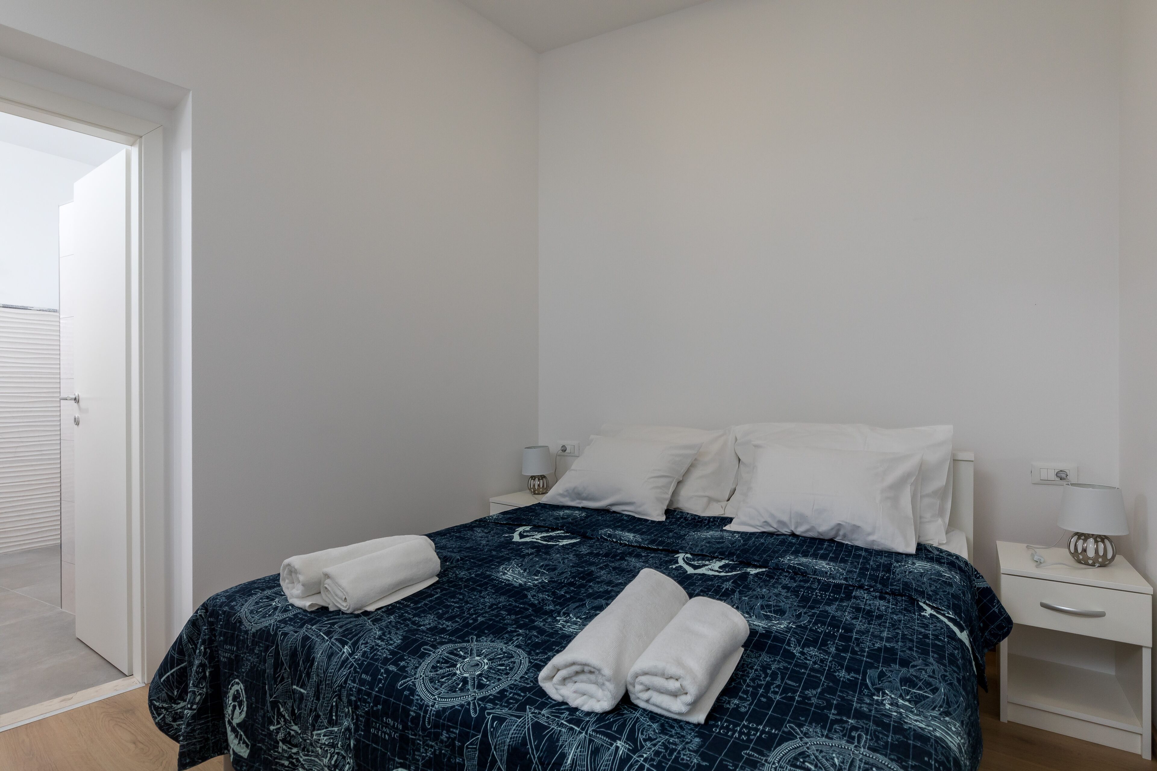 A bedroom with a bed, two bedside tables, a door, and a nightstand with a lamp.
