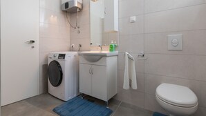 Ett modernt badrum med tvättmaskin, handfat, spegel och toalett.
