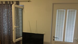Een kamer met een televisie op een wit kastje, een deur met raam en een gordijn met bloemenprint.