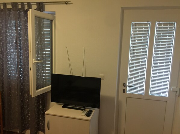 A room with a television on a white cabinet, a door with a window, and a curtain with a floral pattern.
