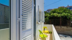 A balcony with a white wall, a window with horizontal blinds, and two yellow chairs.
