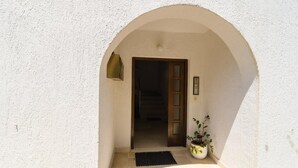 An arched doorway leading into a building, a potted plant on the ground, and a wall-mounted light fixture.