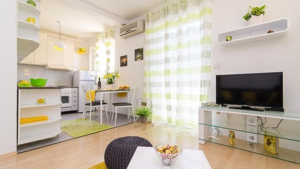 A modern apartment with a kitchen, dining area, and living room. It includes a flat-screen TV, a dining table, chairs, and a sofa.