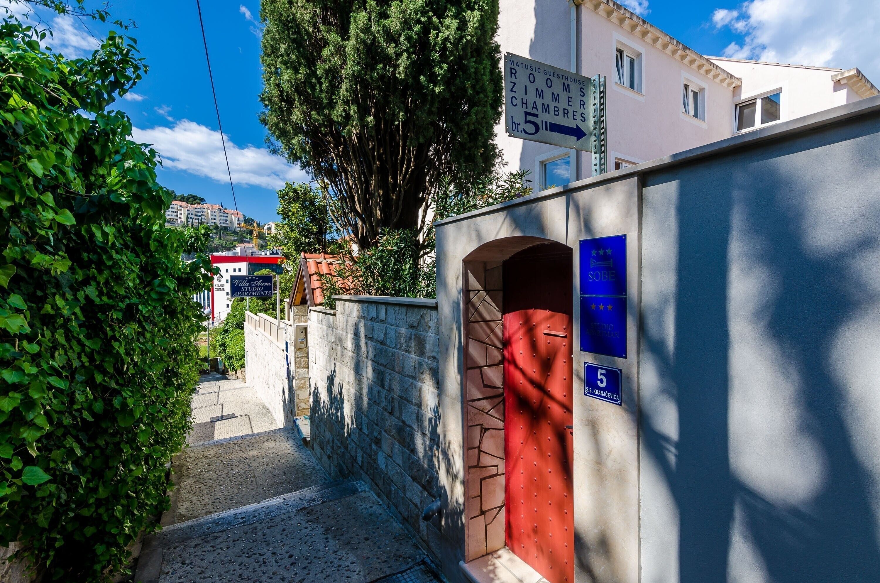 A narrow street with a red door and a sign indicating a guesthouse with rooms and studios.