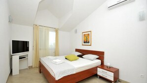 Un dormitorio con cama, televisor, mesita de noche y equipo de aire acondicionado.