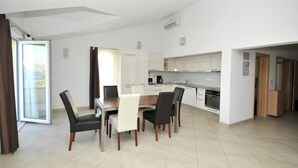Una cocina moderna con armarios blancos, un comedor con mesa y sillas, y un ventanal corredero que da a un balcón.