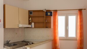 Cozinha com fogão, pia e armários. Há uma janela com cortinas e um aviso na parede.