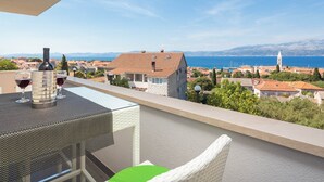A balcony with a table, two wine glasses, and a wine bottle. The view includes a coastal town with buildings and a church.