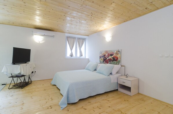 Ein Schlafzimmer mit einem Bett, einem Fernseher auf einem Schrank, einem kleinen Nachttisch und einem Fenster mit Vorhängen.