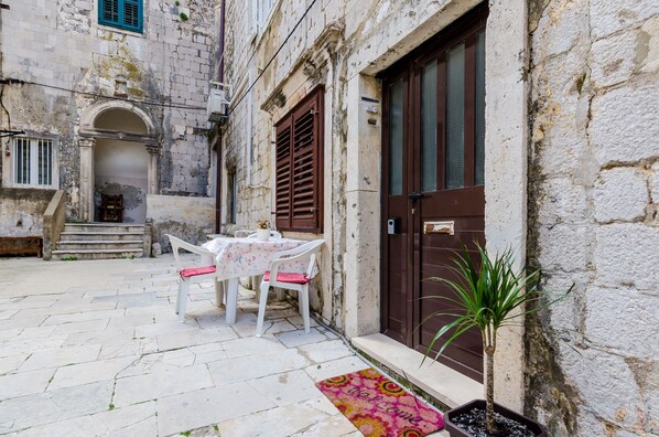 A courtyard with a table and chairs, a potted plant, and a door.