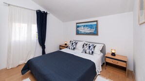 Une chambre à coucher avec un lit, deux tables de chevet, une commode, une fenêtre avec des rideaux et un tableau au mur.