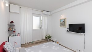 A bedroom with a bed, a TV, a desk, and a window with curtains. - Room Primi - Double Room with Terrace (Dubrovnik)
