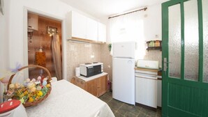 Une cuisine de taille réduite avec des meubles blancs, un réfrigérateur blanc, une porte verte et un panier rempli d’objets colorés posé sur la table.