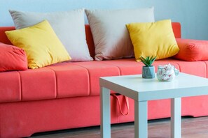 A red sofa with multiple pillows in various colors, a small table with a plant and a glass jar, and a red bag on the sofa. - Captain's Studio - Studio with Terrace (Mokosica)
