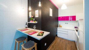 Een compacte keuken met een zwarte accentmuur, witte kasten en een kleine eethoek met krukken.