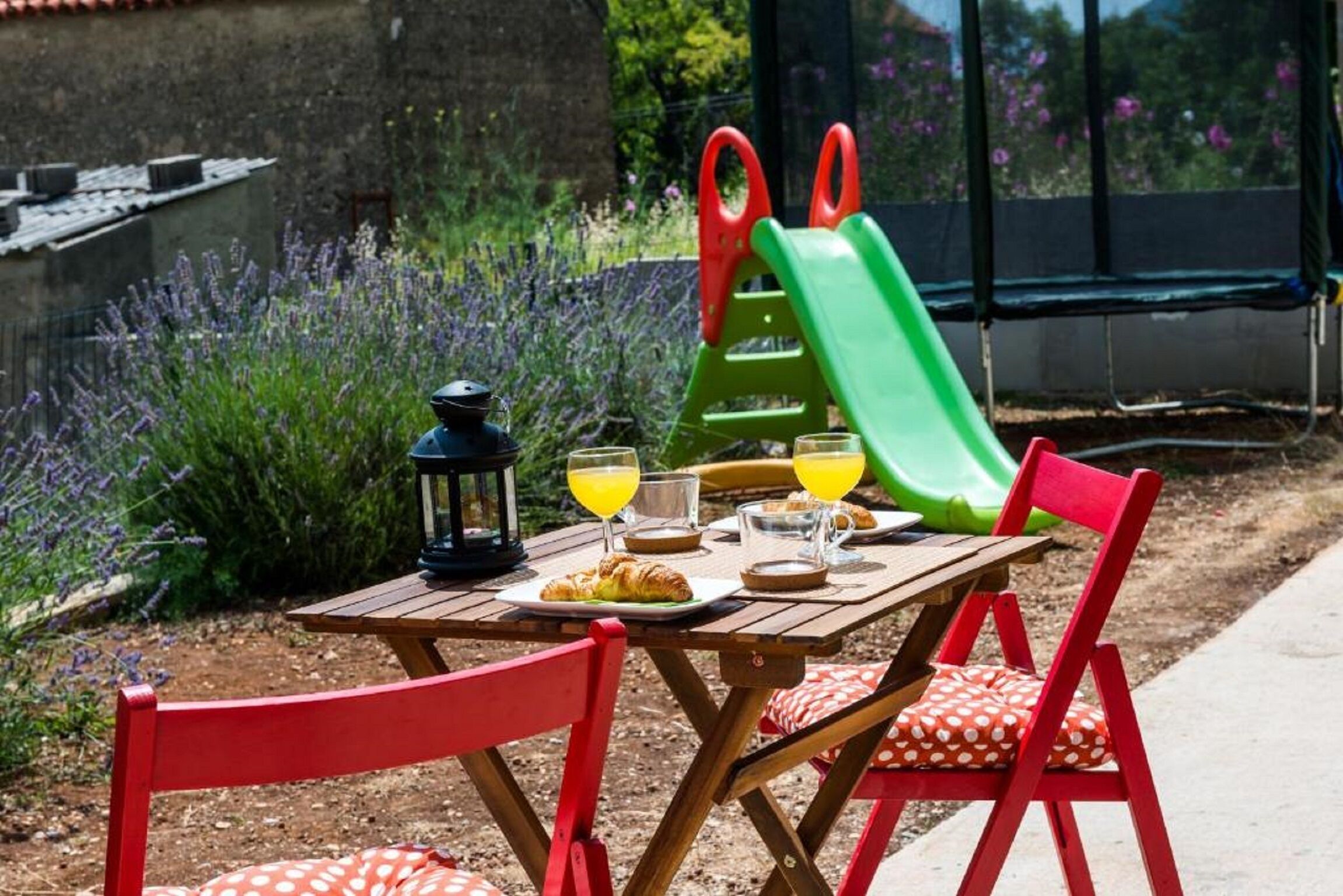 A wooden table with a picnic setup, including a plate of food, glasses of orange juice, and a lantern.