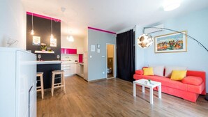 Een moderne woonkamer met een rode bank, een witte salontafel en een keukenhoek met een roze accentmuur.