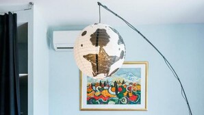 Een kamer met een rode bank, een witte salontafel, een wereldbol die aan het plafond hangt, en een kleurrijk schilderij aan de muur.