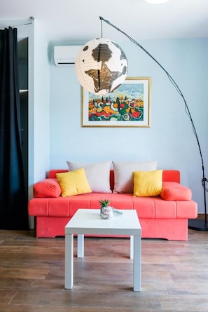 Une pièce avec un canapé rouge, une table basse blanche, un globe suspendu au plafond et un tableau coloré accroché au mur.