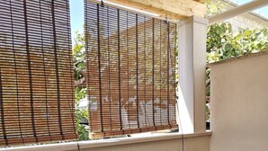Ein überdachter Patio-Bereich mit Tisch und Stühlen, Bambusrollos und Blick ins Grüne.