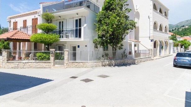 Un immeuble de deux étages doté de balcons, d’un mur en pierre et d’une voiture garée.