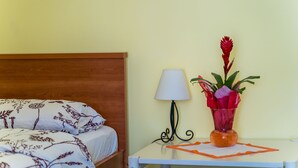 A neatly made bed with floral bedding, a bedside lamp, and a vase with flowers on a small table. - Rooms Katja & Lara - Twin Room (Dubrovnik)