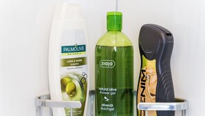 A bathroom shelf with a bottle of Palmolive shampoo, a bottle of natural olive shower gel, and a black hairdryer. - Rooms Katja & Lara - Twin Room (Dubrovnik)